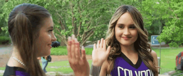 two cheerleaders are giving each other a high five and one of them is wearing a purple uniform that says colvard