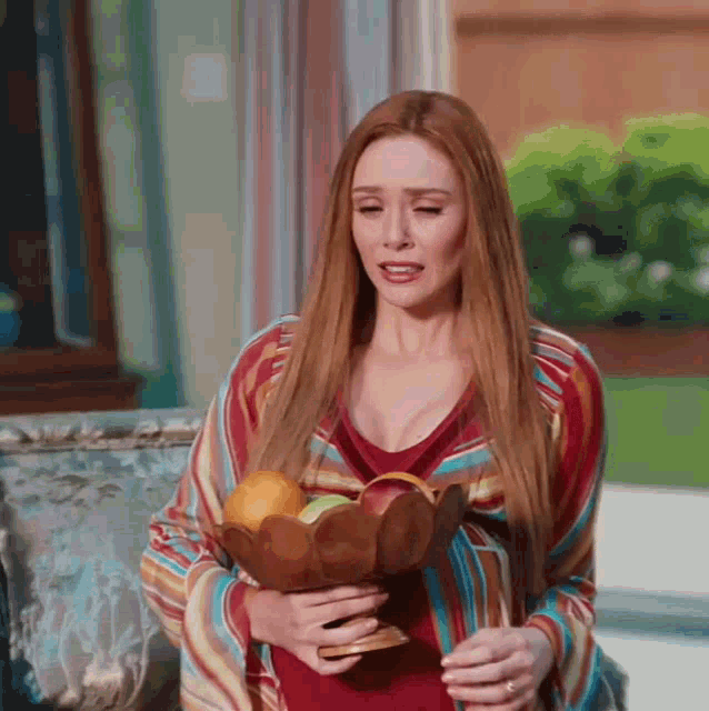 a woman is holding a bowl of fruit in her hands and making a funny face .