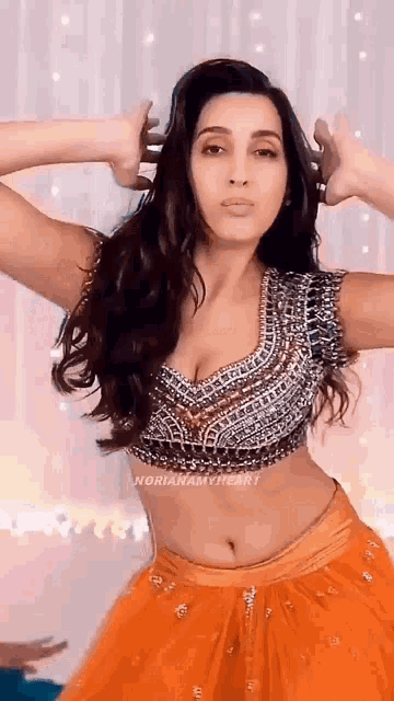 a woman in a crop top and orange skirt is dancing with her hands in her hair .