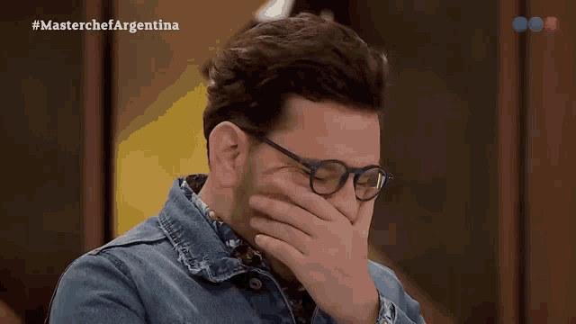 a man wearing glasses covering his face with his hand while watching a masterchef argentina show