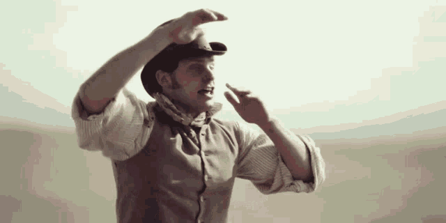 a man in a cowboy hat and vest is making a gesture with his hands