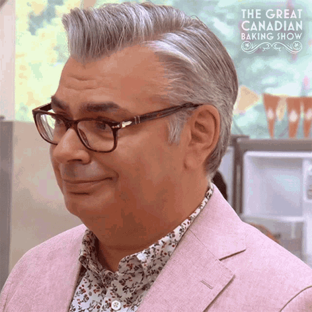 a man wearing glasses and a pink jacket with the great canadian baking show behind him