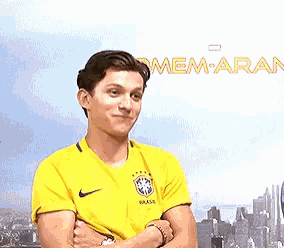 a man in a yellow shirt is standing with his arms crossed in front of a city .