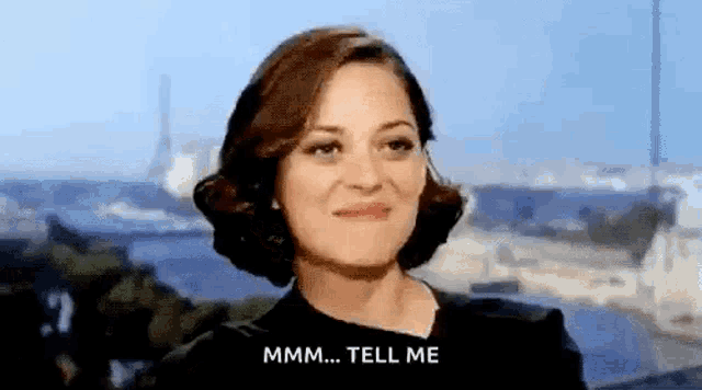 a woman is smiling and saying `` mmmm ... tell me '' while standing in front of a body of water .