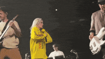 a woman wearing a yellow sweatshirt that says nyc pain on it