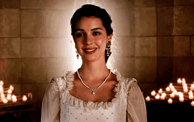 a woman wearing a white dress and a pearl necklace smiles in front of candles