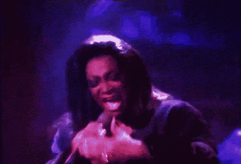 a woman singing into a microphone in a dark room with purple lights