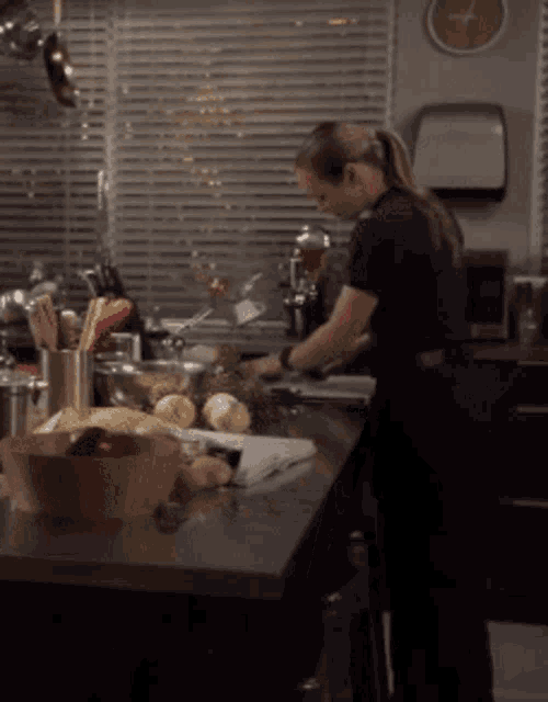 a woman prepares food in a kitchen with a clock on the wall above her