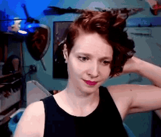 a woman in a black tank top holds her hair up
