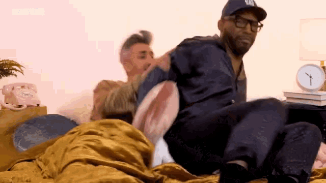 a man wearing a ny hat is sitting on a bed with another man