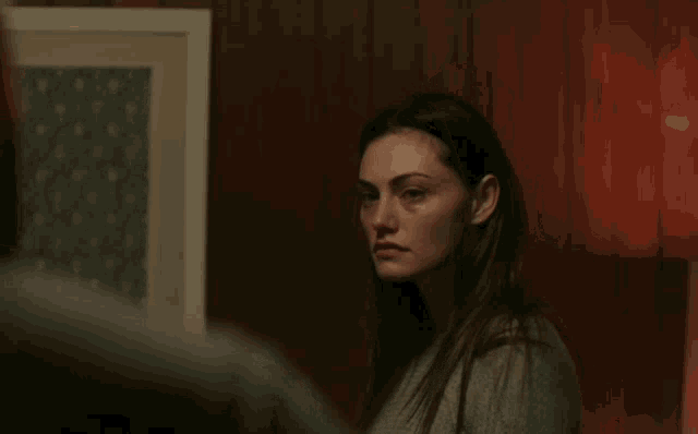 a woman in a gray sweater stands in front of a wooden wall