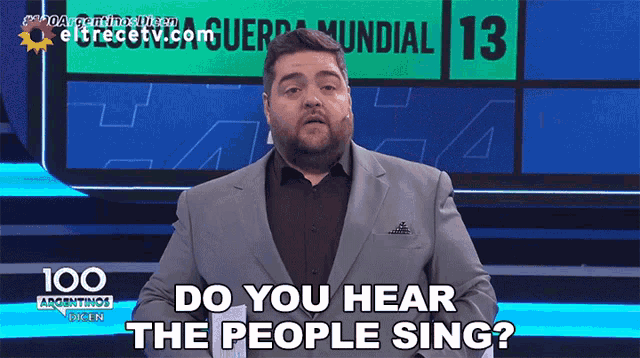 a man in a suit stands in front of a sign that says do you hear the people sing