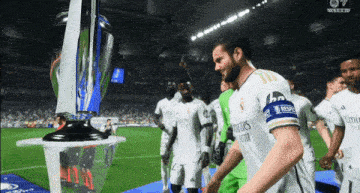 a soccer player wearing a jersey that says fly emirates better stands in front of a trophy