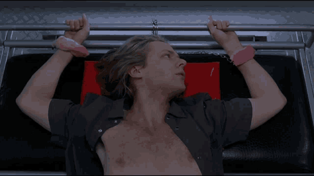 a shirtless man with pink handcuffs is laying on a bed