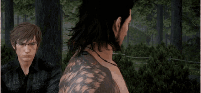 two men are standing next to each other in the woods . one of the men has a tattoo on his back .