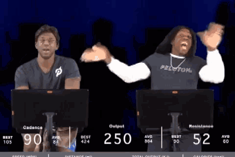 a man wearing a peloton shirt is standing next to another man on a treadmill