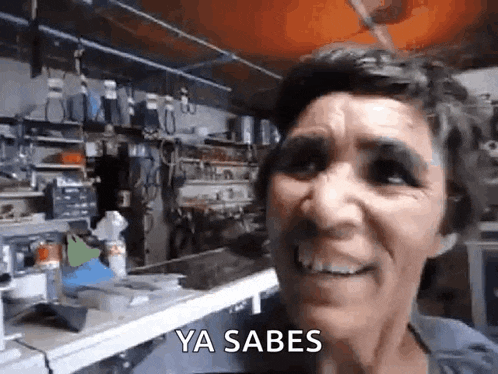 a woman is smiling while standing in a garage with the words ya sabes written on her face .
