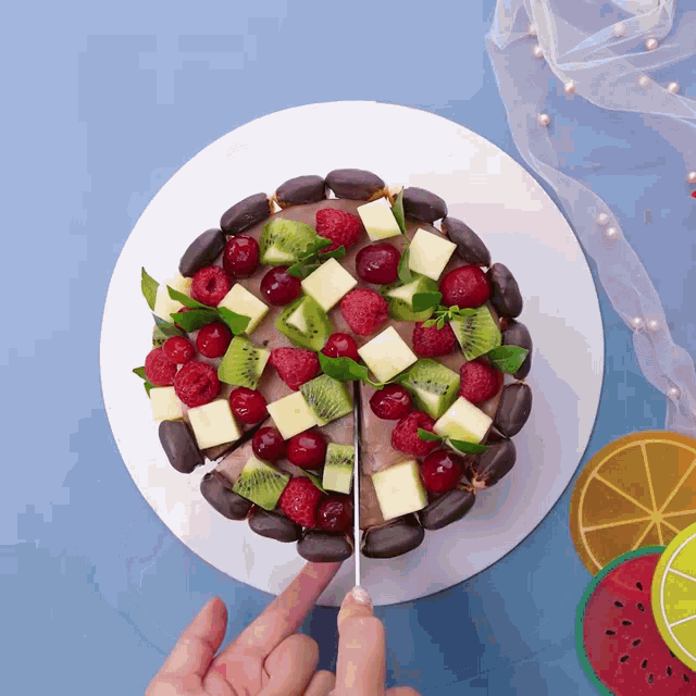 a person is cutting a cake with fruit on it with a knife