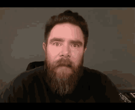 a man with a beard and mustache is making a funny face while looking at the camera .