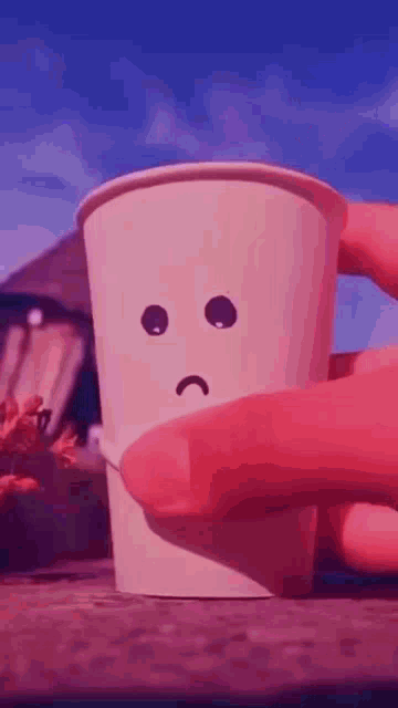 a cup with a sad face drawn on it is being held by a person .