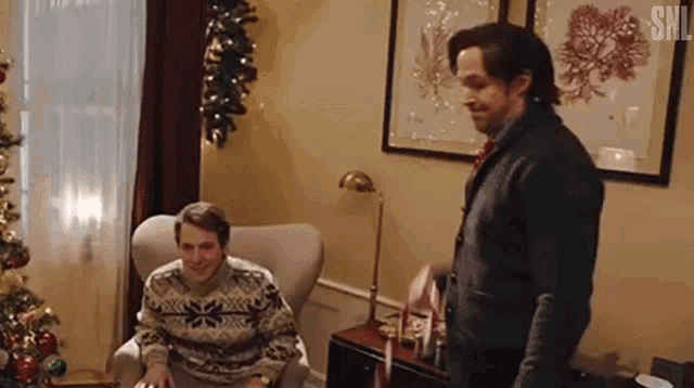 two men are standing in a living room with a christmas tree in the background .