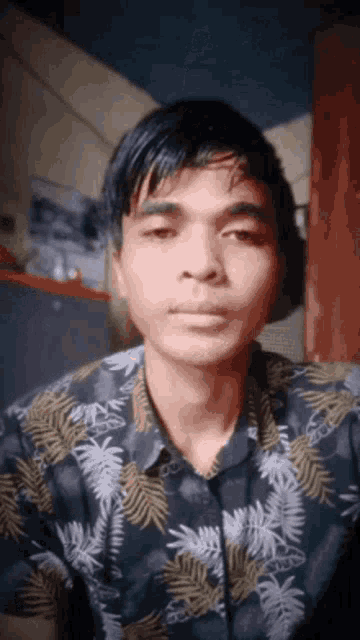 a young man wearing a hawaiian shirt is looking at the camera .