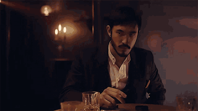 a man in a suit sitting at a table with a glass of whiskey