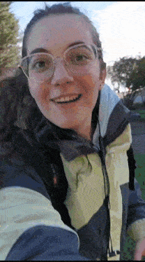 a woman wearing glasses and a jacket is taking a selfie .