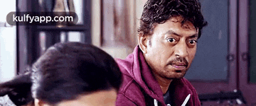 a man in a purple hoodie is sitting at a table with a woman behind him .