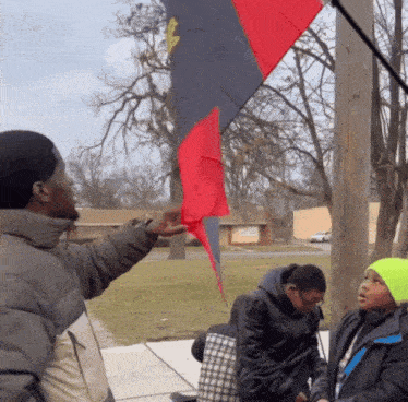 a man pointing at a red and black flag with a yellow flower on it
