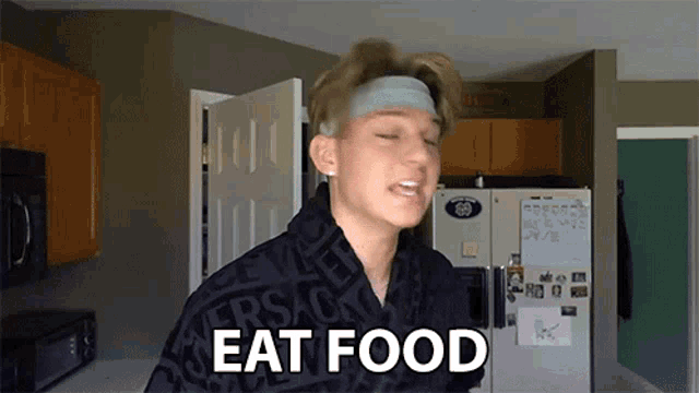 a young man wearing a headband says eat food in front of a refrigerator