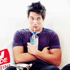 a man drinking from a bottle with a straw while sitting on a couch in front of a magazine