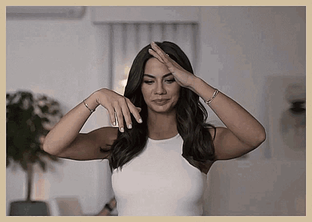 a woman in a white tank top holds her hand to her head