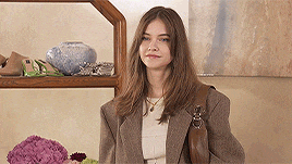 a woman in a brown jacket is standing in front of a shelf with shoes on it .