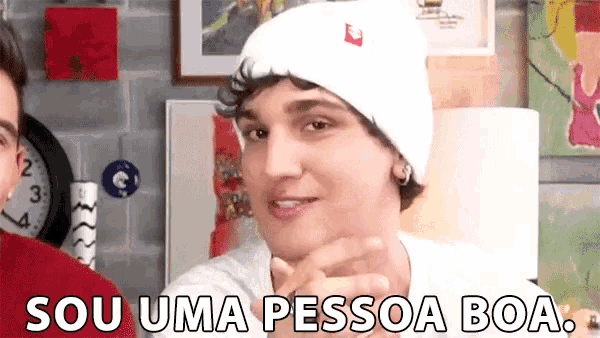 a man wearing a white hat and a white shirt is pointing at the camera and says `` sou uma pessoa boa '' .