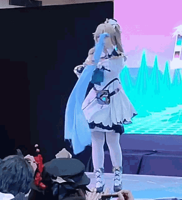 a woman in a cosplay costume is standing on a stage holding a blue scarf .