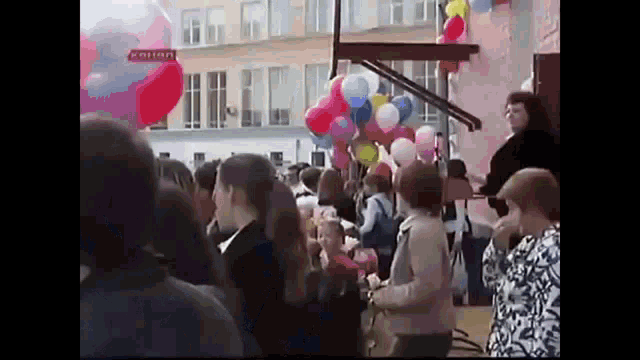a crowd of people are gathered in front of a building with balloons flying in the air