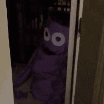 a purple stuffed animal with big eyes is standing in a doorway .
