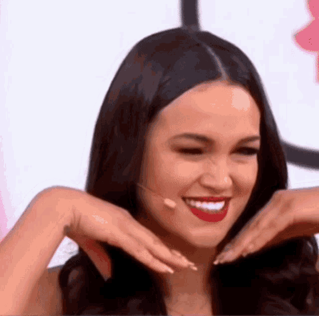 a woman with red lipstick is smiling and making a funny face with her hands .
