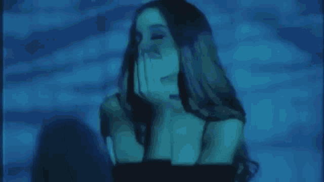 a woman is covering her face with her hand in a dark room with a blue light projected on her face .
