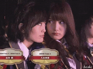 a couple of girls sitting next to each other with a badge that says akb48 team a