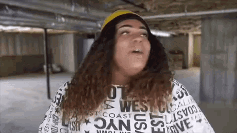a woman with long curly hair is wearing a hat and a t-shirt that says west coast on it .