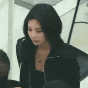 a woman with long black hair is wearing a black jacket and a necklace .