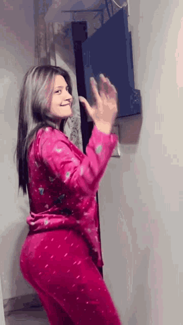 a woman in a pink pajama set is standing in front of a television and waving .