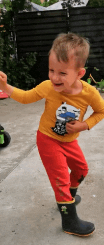 a little boy wearing a yellow shirt and red pants is standing on a sidewalk
