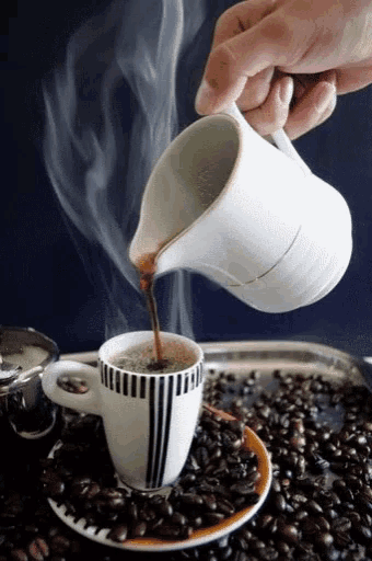 a cup of coffee is being poured from a pitcher onto a saucer surrounded by coffee beans