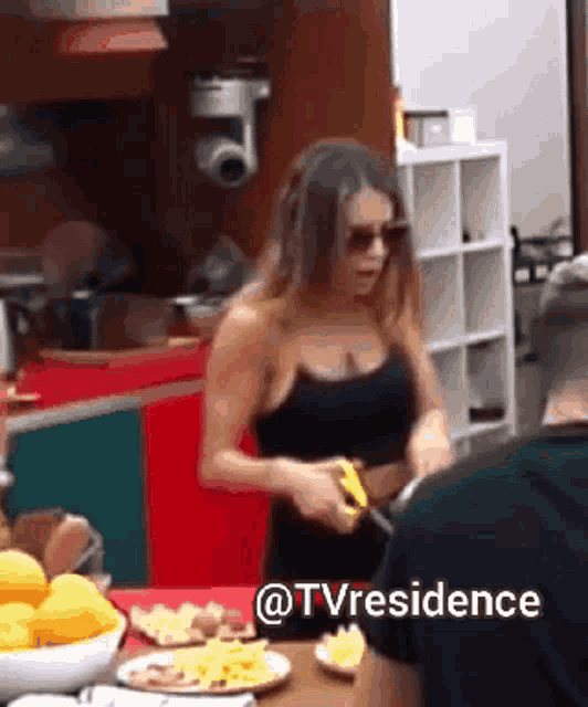 a woman in a black top is standing in front of a table with plates of food and a sign that says tv residence
