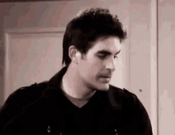 a man in a black jacket is standing in front of a door and looking down .