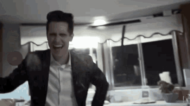 a man in a suit and white shirt is laughing in a kitchen with his arms outstretched .