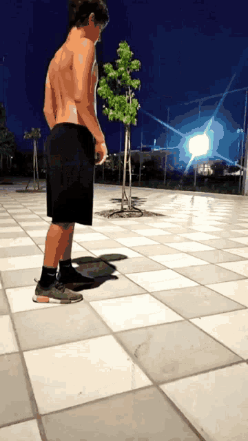 a man without a shirt is standing on a tiled floor in front of a tree
